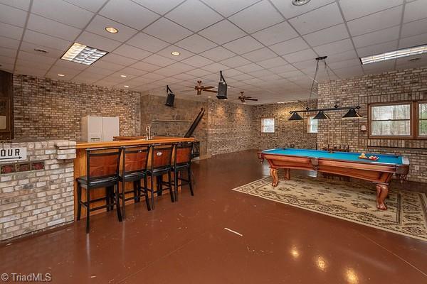 game room with concrete flooring, pool table, indoor wet bar, brick wall, and a drop ceiling