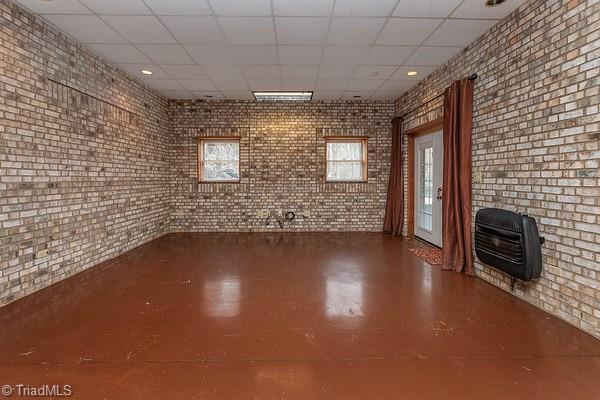 interior space featuring brick wall, heating unit, a paneled ceiling, and concrete floors