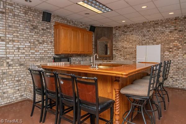 bar featuring brick wall, sink, and a paneled ceiling