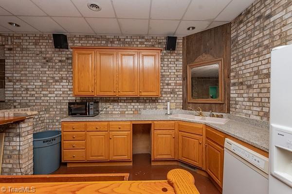 kitchen with a paneled ceiling, brick wall, white dishwasher, and sink