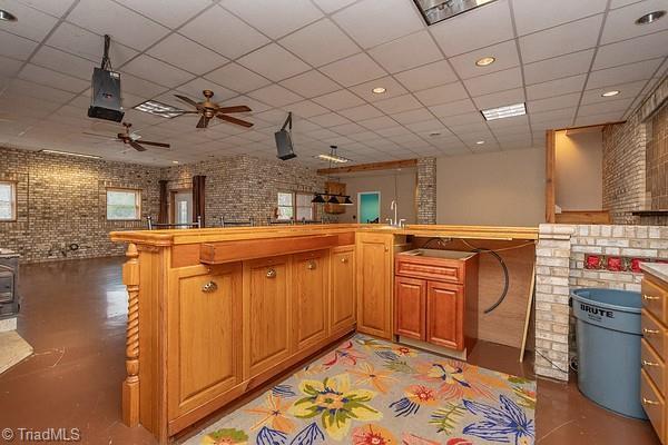 kitchen featuring sink, brick wall, a drop ceiling, kitchen peninsula, and a wood stove