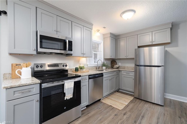 kitchen with gray cabinetry, light hardwood / wood-style flooring, a textured ceiling, appliances with stainless steel finishes, and light stone counters