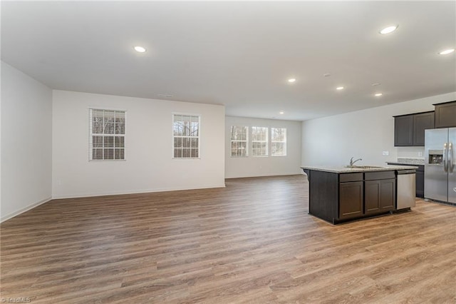 kitchen featuring light countertops, appliances with stainless steel finishes, open floor plan, a sink, and light wood-type flooring