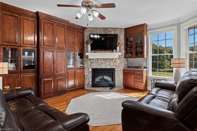 living area featuring ceiling fan, light wood finished floors, a fireplace, and crown molding