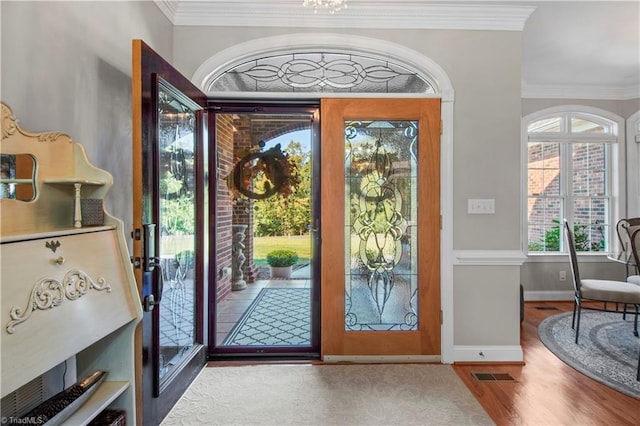 foyer entrance featuring ornamental molding, visible vents, baseboards, and wood finished floors