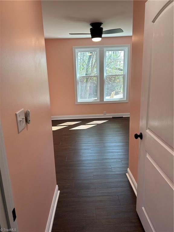 interior space with baseboards, a ceiling fan, and dark wood finished floors