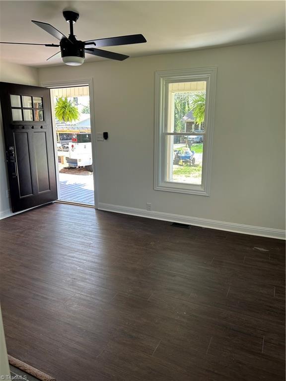 interior space with dark wood-style flooring, baseboards, a ceiling fan, and visible vents