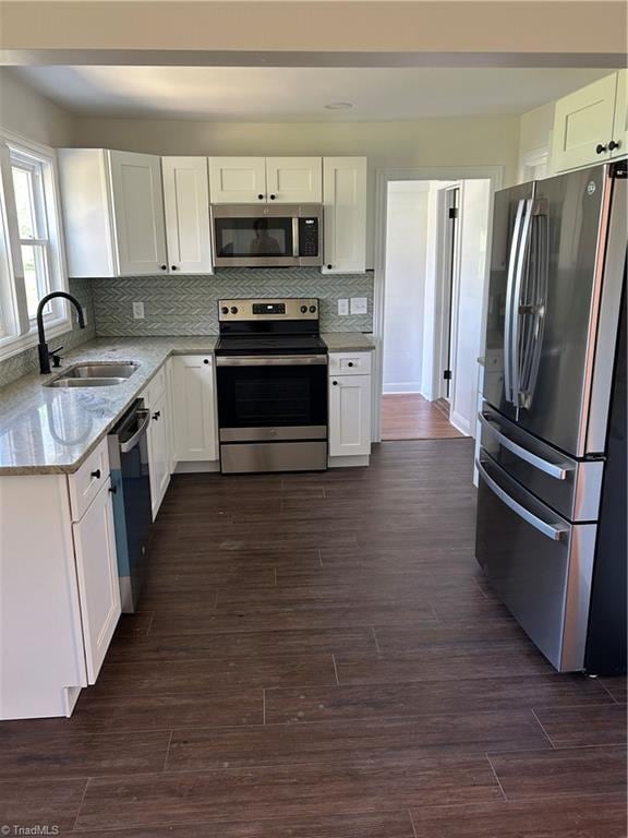 kitchen with white cabinets, appliances with stainless steel finishes, light stone counters, a sink, and dark wood-style floors
