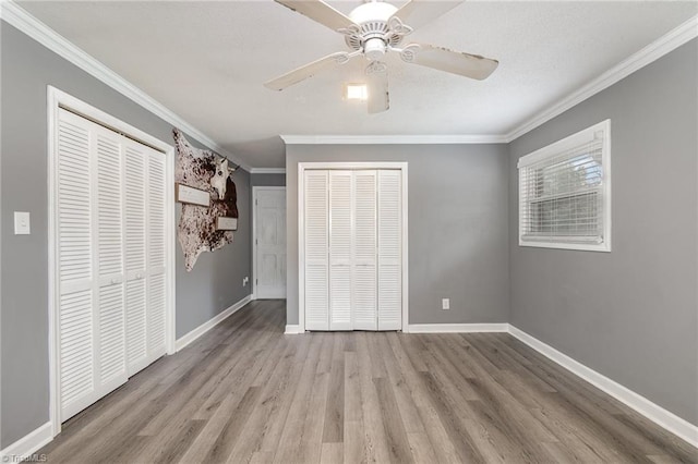 unfurnished bedroom with ceiling fan, ornamental molding, two closets, and light hardwood / wood-style floors