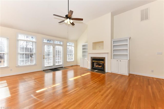 unfurnished living room with vaulted ceiling, built in features, ceiling fan, a fireplace, and light hardwood / wood-style floors