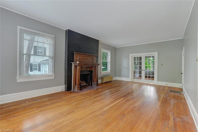 unfurnished living room featuring radiator, ornamental molding, french doors, a fireplace, and light wood-type flooring