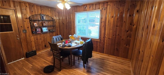 dining space with wood walls, ceiling fan, and wood finished floors