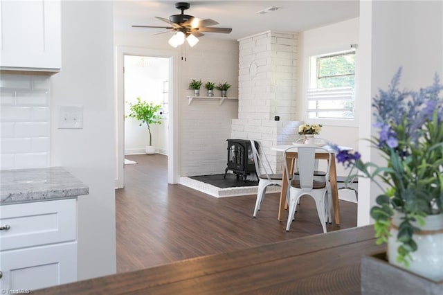 dining room featuring ornate columns, ceiling fan, dark hardwood / wood-style flooring, and a wood stove