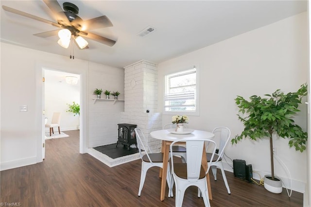 dining room with ceiling fan, dark hardwood / wood-style flooring, and a wood stove