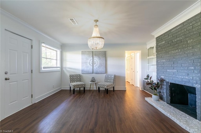 sitting room with a brick fireplace, dark hardwood / wood-style floors, a notable chandelier, ornamental molding, and built in shelves