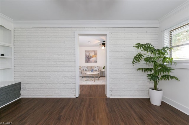 spare room featuring brick wall, crown molding, dark wood-type flooring, and ceiling fan