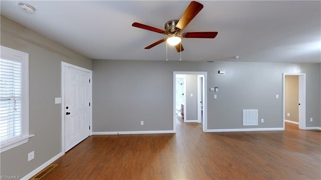 empty room with ceiling fan, a healthy amount of sunlight, and dark hardwood / wood-style flooring