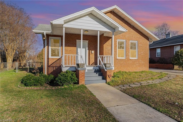 view of front of home with brick siding, fence, a porch, and a front yard