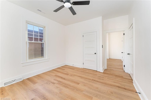 empty room featuring ceiling fan, light wood finished floors, visible vents, and baseboards