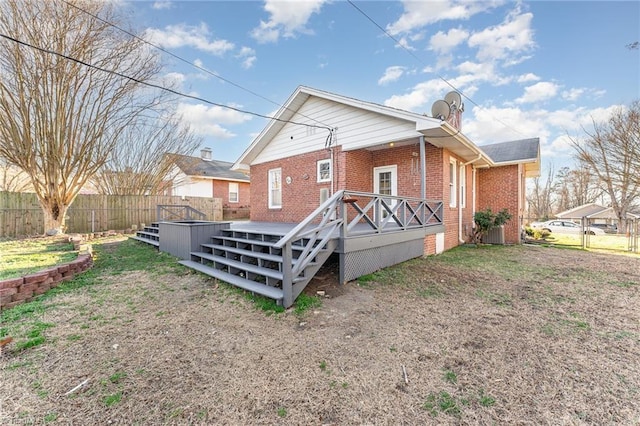 back of property featuring a wooden deck, fence, a lawn, and brick siding