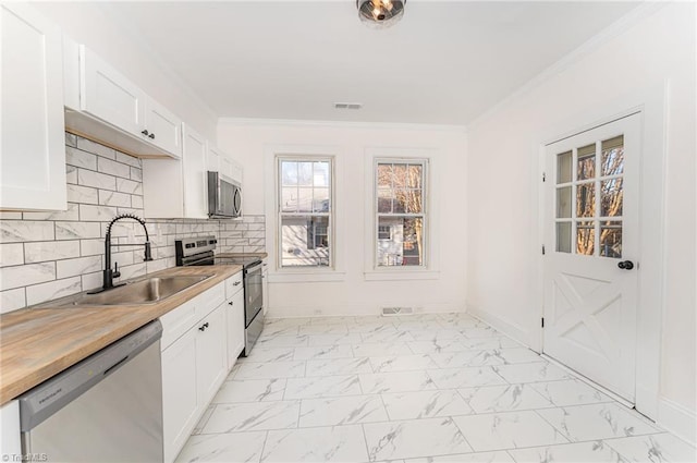 kitchen with marble finish floor, stainless steel appliances, ornamental molding, white cabinets, and a sink