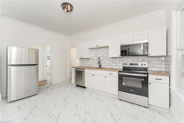 kitchen featuring butcher block countertops, marble finish floor, stainless steel appliances, crown molding, and a sink