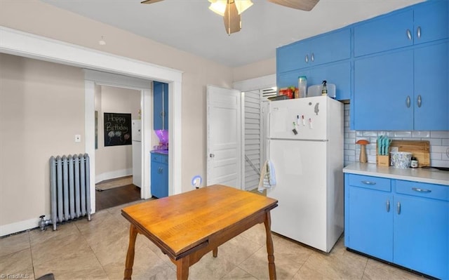 kitchen with tasteful backsplash, blue cabinetry, white fridge, radiator heating unit, and ceiling fan