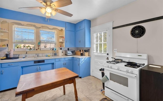 kitchen featuring decorative backsplash, light tile patterned floors, ceiling fan, blue cabinetry, and gas range gas stove