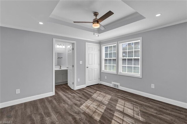 unfurnished bedroom featuring dark wood-type flooring, ensuite bath, a raised ceiling, and ceiling fan