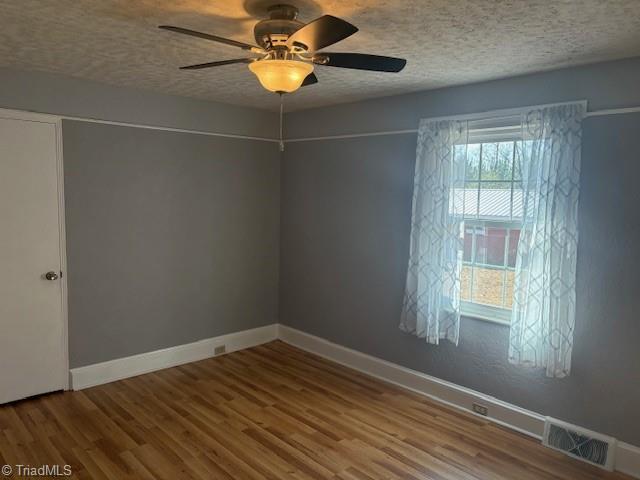 empty room with a textured ceiling, hardwood / wood-style flooring, and ceiling fan