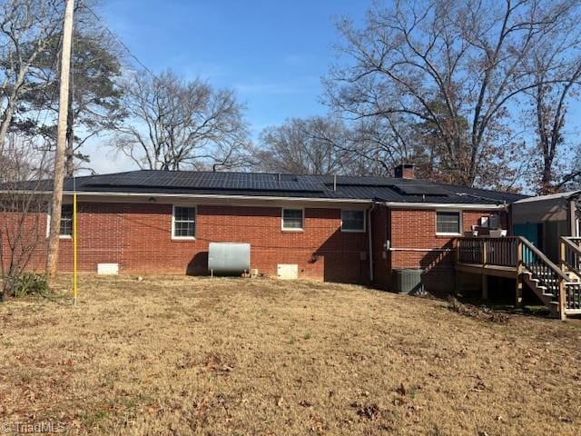 back of house with solar panels, a wooden deck, and a lawn