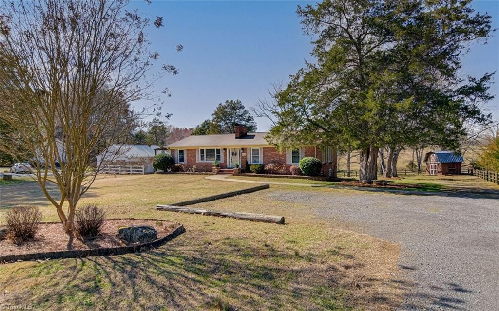 view of front of house featuring brick siding, an outdoor structure, fence, a shed, and a front yard