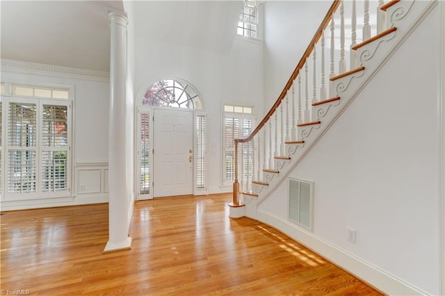 entryway featuring a towering ceiling, light wood-type flooring, and decorative columns