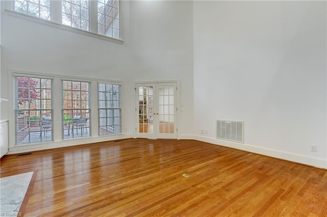 unfurnished living room featuring a towering ceiling, french doors, and light wood-type flooring