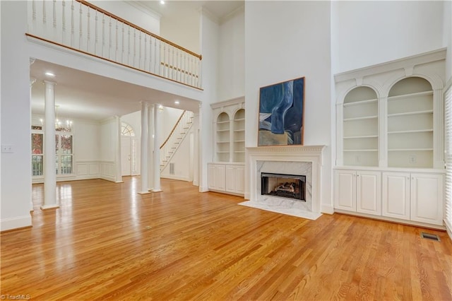 unfurnished living room with a fireplace, built in shelves, light hardwood / wood-style flooring, and a high ceiling