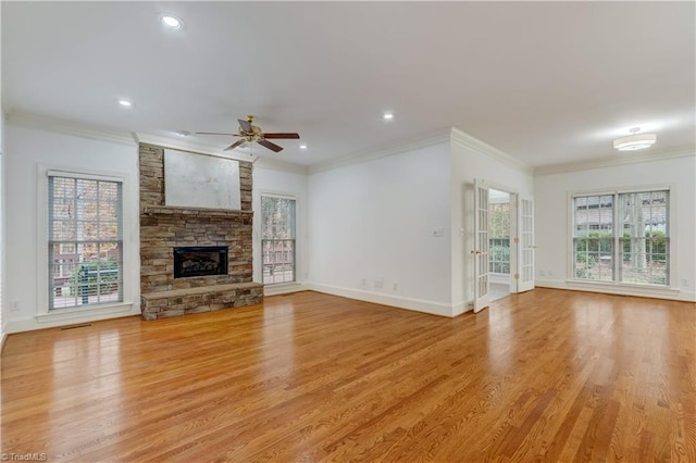 unfurnished living room with crown molding, a wealth of natural light, a fireplace, and light hardwood / wood-style floors