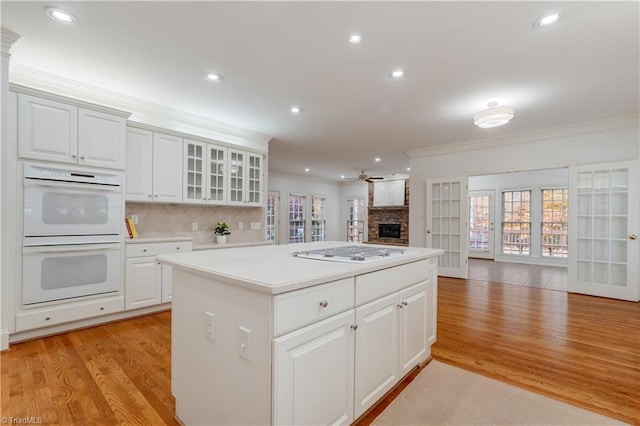 kitchen with white double oven, white cabinets, light wood-type flooring, ornamental molding, and gas cooktop