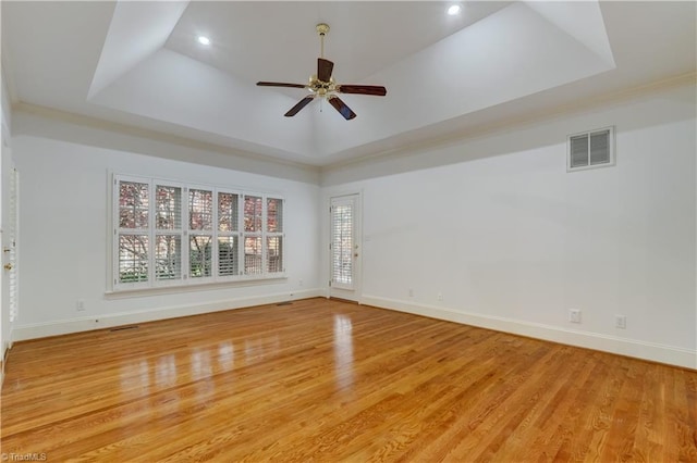 empty room with light hardwood / wood-style floors, ceiling fan, and a tray ceiling