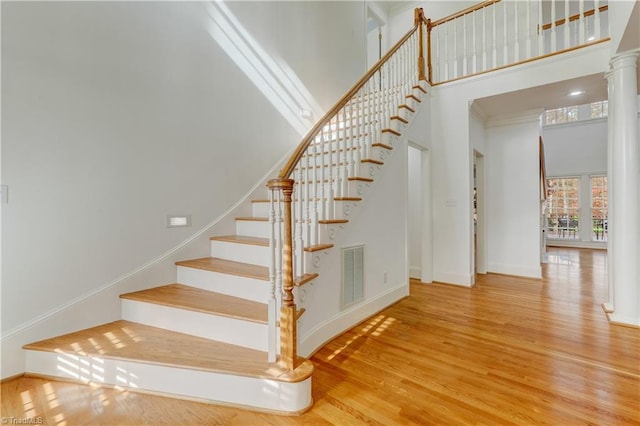 stairway featuring hardwood / wood-style floors, a towering ceiling, and decorative columns