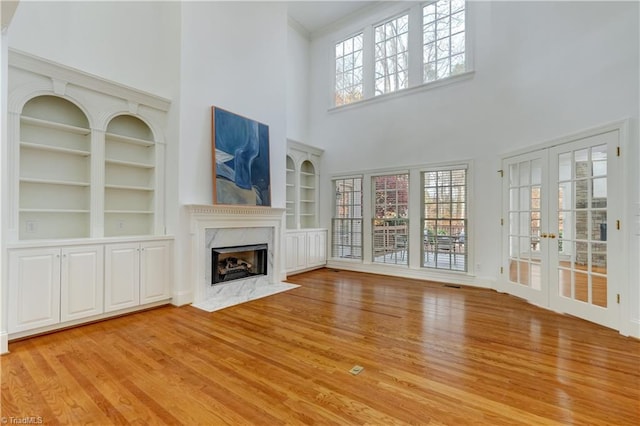 unfurnished living room featuring french doors, light hardwood / wood-style flooring, built in features, a fireplace, and a towering ceiling