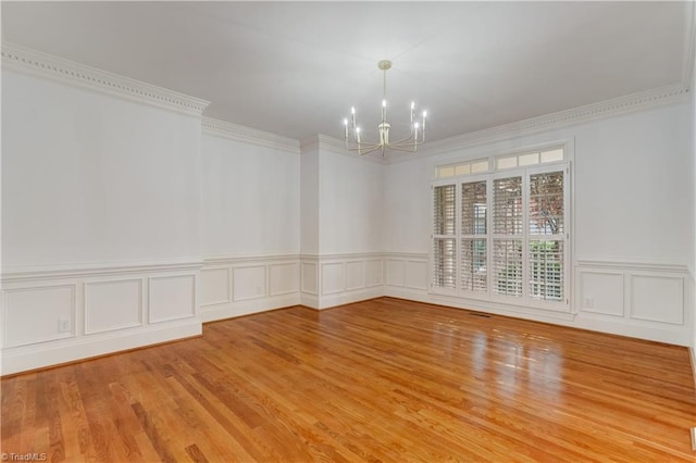 spare room featuring crown molding, wood-type flooring, and an inviting chandelier