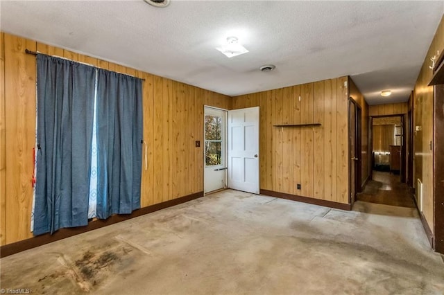 carpeted empty room featuring wooden walls and a textured ceiling