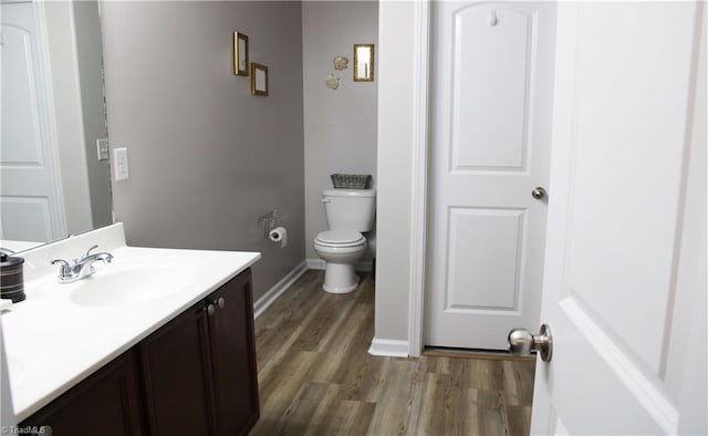 bathroom featuring baseboards, toilet, wood finished floors, and vanity