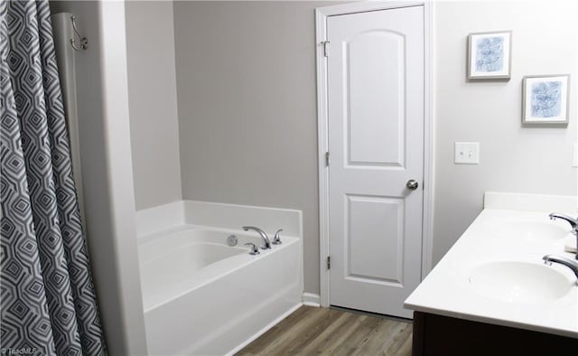 full bathroom with a sink, a garden tub, wood finished floors, and double vanity