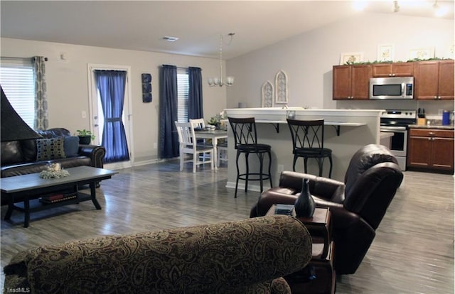 living area featuring an inviting chandelier, wood finished floors, baseboards, and vaulted ceiling