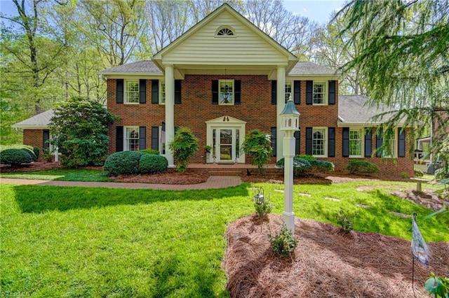 neoclassical / greek revival house with roof with shingles, a front lawn, and brick siding