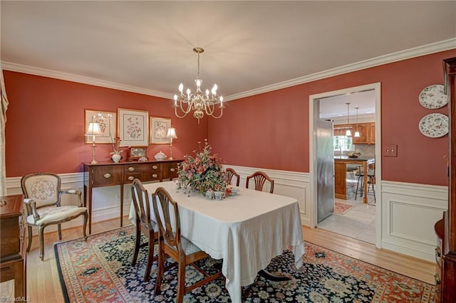 dining space with light wood-style floors, a wainscoted wall, an inviting chandelier, and ornamental molding