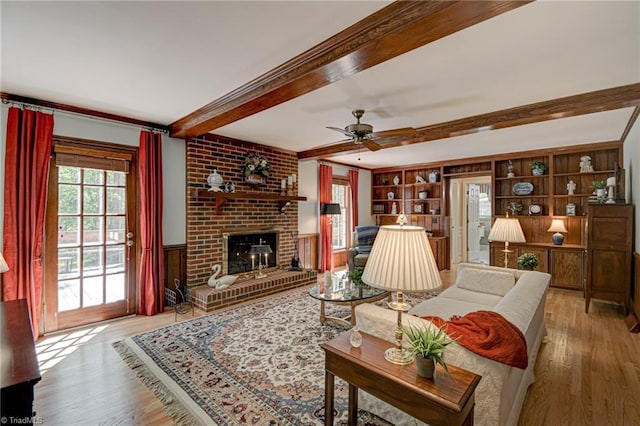 living area featuring a ceiling fan, a brick fireplace, wood finished floors, and beamed ceiling