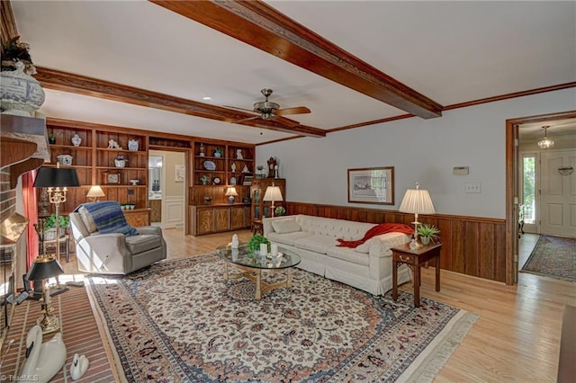 living area with wainscoting, light wood finished floors, a ceiling fan, beamed ceiling, and ornamental molding