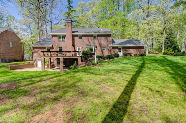 rear view of house featuring a chimney, brick siding, a yard, and a deck